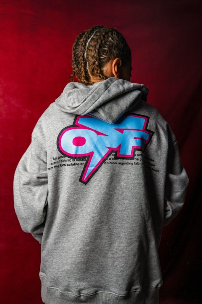 A person with braided hair wearing a grey hoodie with a blue and pink graphic
